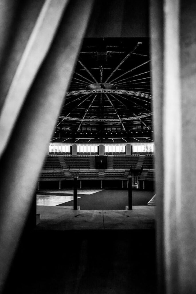 A black and white image capturing an empty arena stage viewed through curtains.